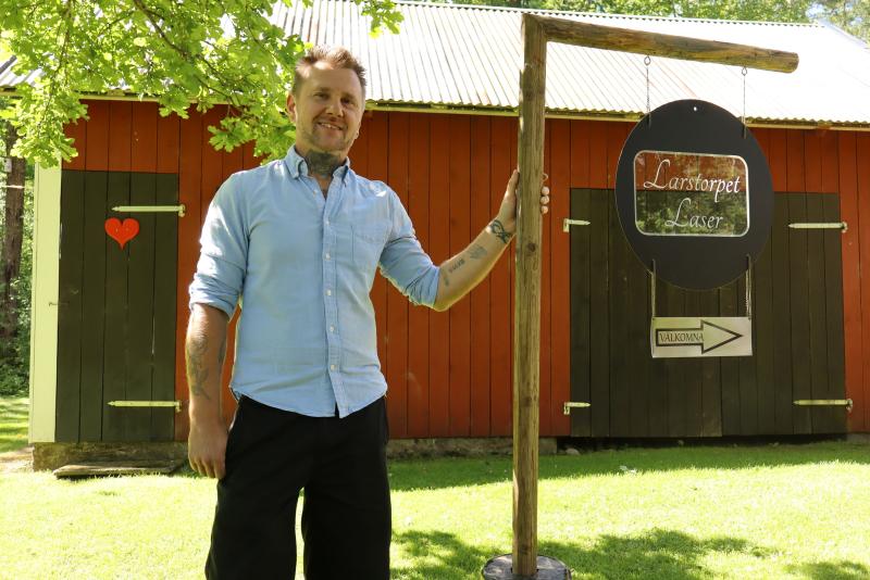 En person står ute på gräset bredvid en träskylt med texten 