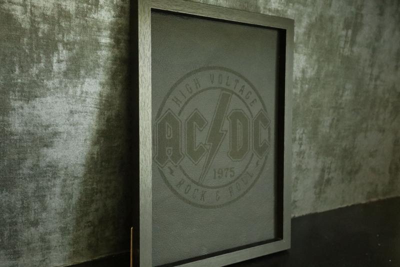 Ett inramat konstverk med AC/DC:s logotyp och texten 