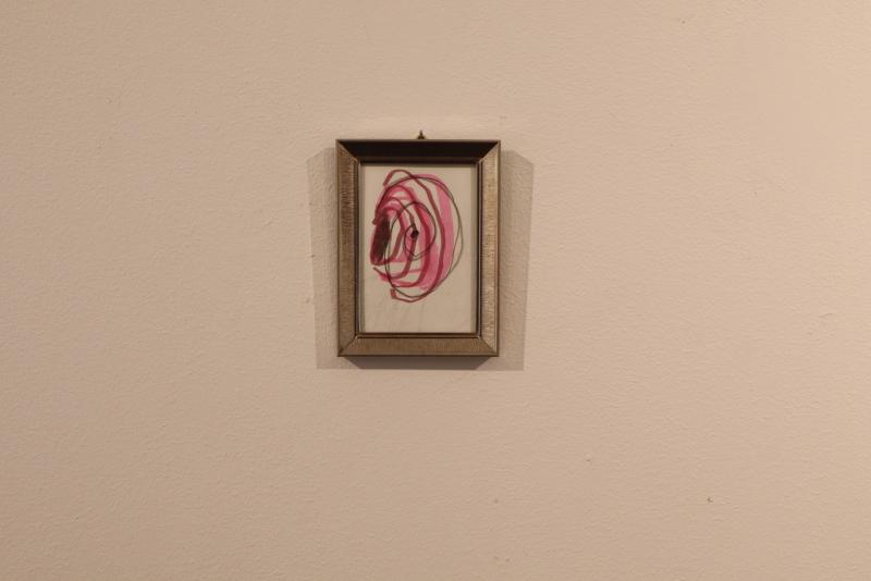 På en ljusbeige vägg hänger en liten inramad tavla med en abstrakt rosa spiralmönster med några mörkare markeringar i mitten.