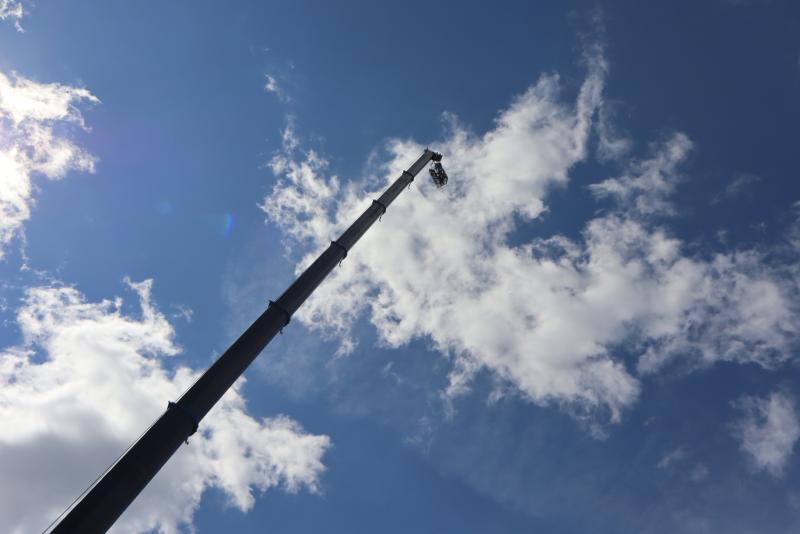 En kran med en korg sträcker sig högt upp mot himlen mot en bakgrund av spridda moln och blå himmel.