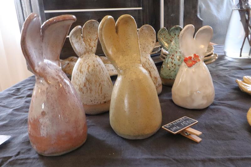 Kaninfigurer i keramik i olika färger står upprätt på en mörk duk, och en av figurerna har en liten röd blomdekoration.